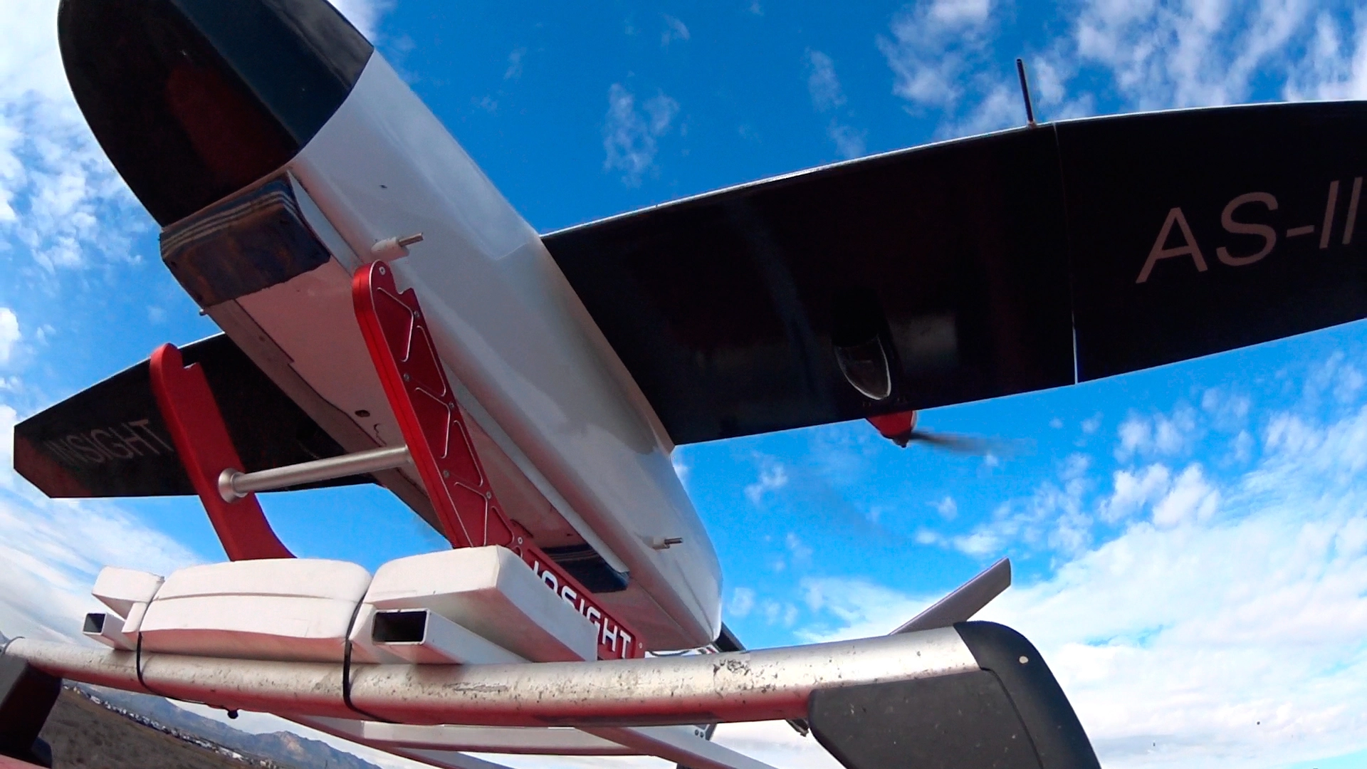 Underneath view of the AS-III UAS showcasing its wings and launch mechanism against a blue sky.